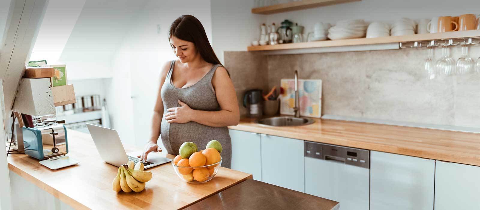 Pregnant woman viewing laptop in kitchen.