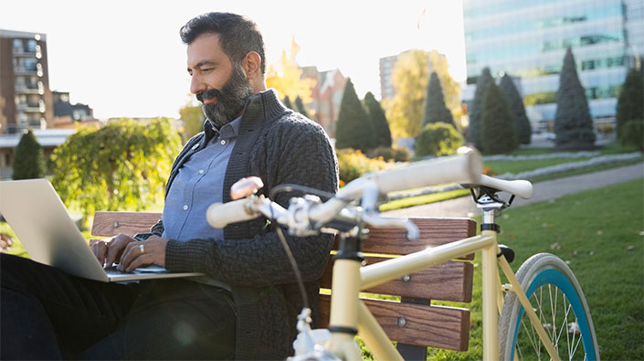 Middle aged man outdoors using laptop on park bench