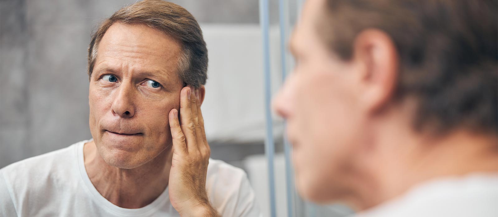 Middle aged man examining his face on mirror.