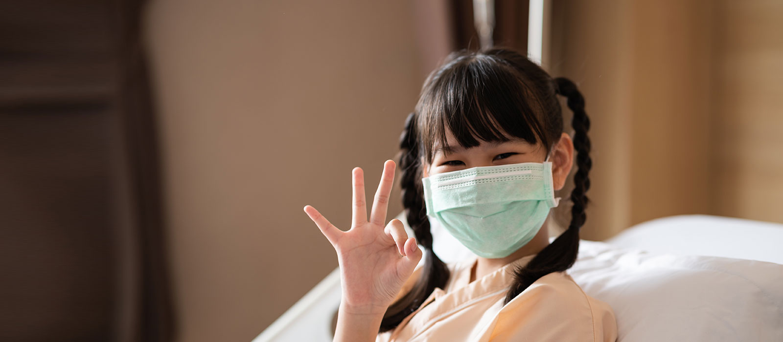 young girl wearing protective mask in hospital bed