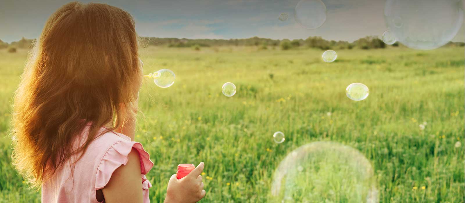 Young girl blowing bubbles in green field