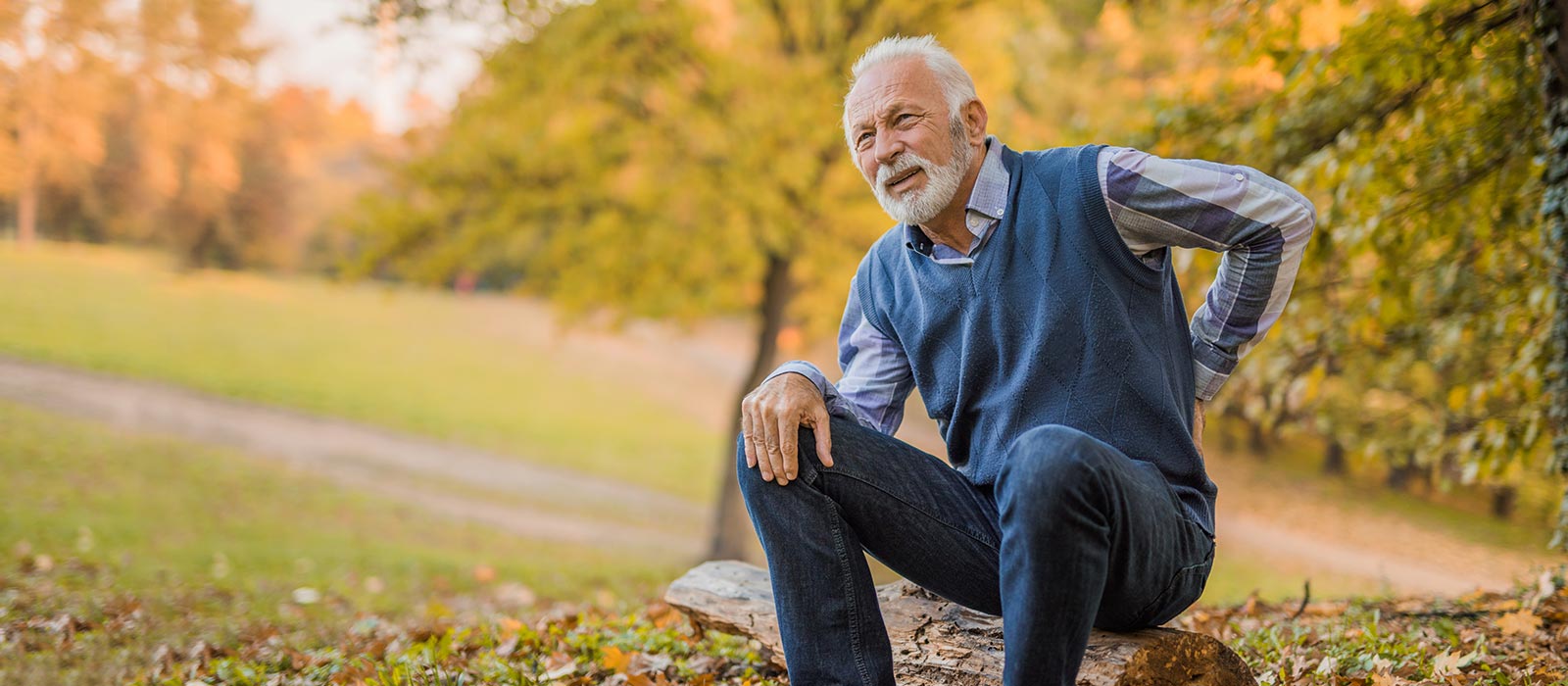 older man outside holding his sore back