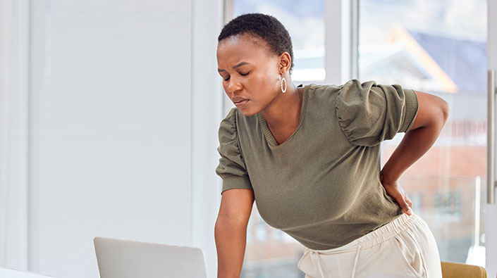 professional woman standing up at desk with hand on back