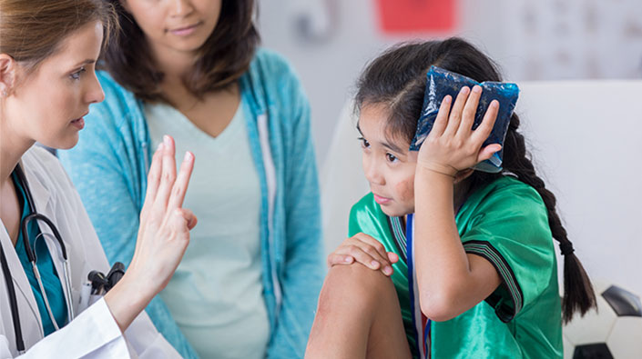 girl holding ice pack to her head while doctor holds up 3 fingers