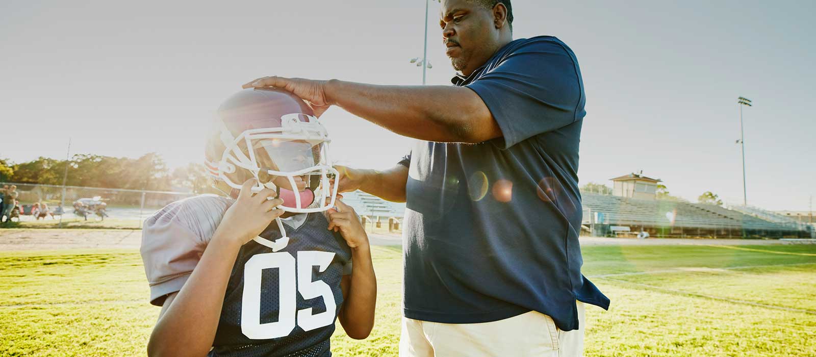 Youth football player's parent help with helmet