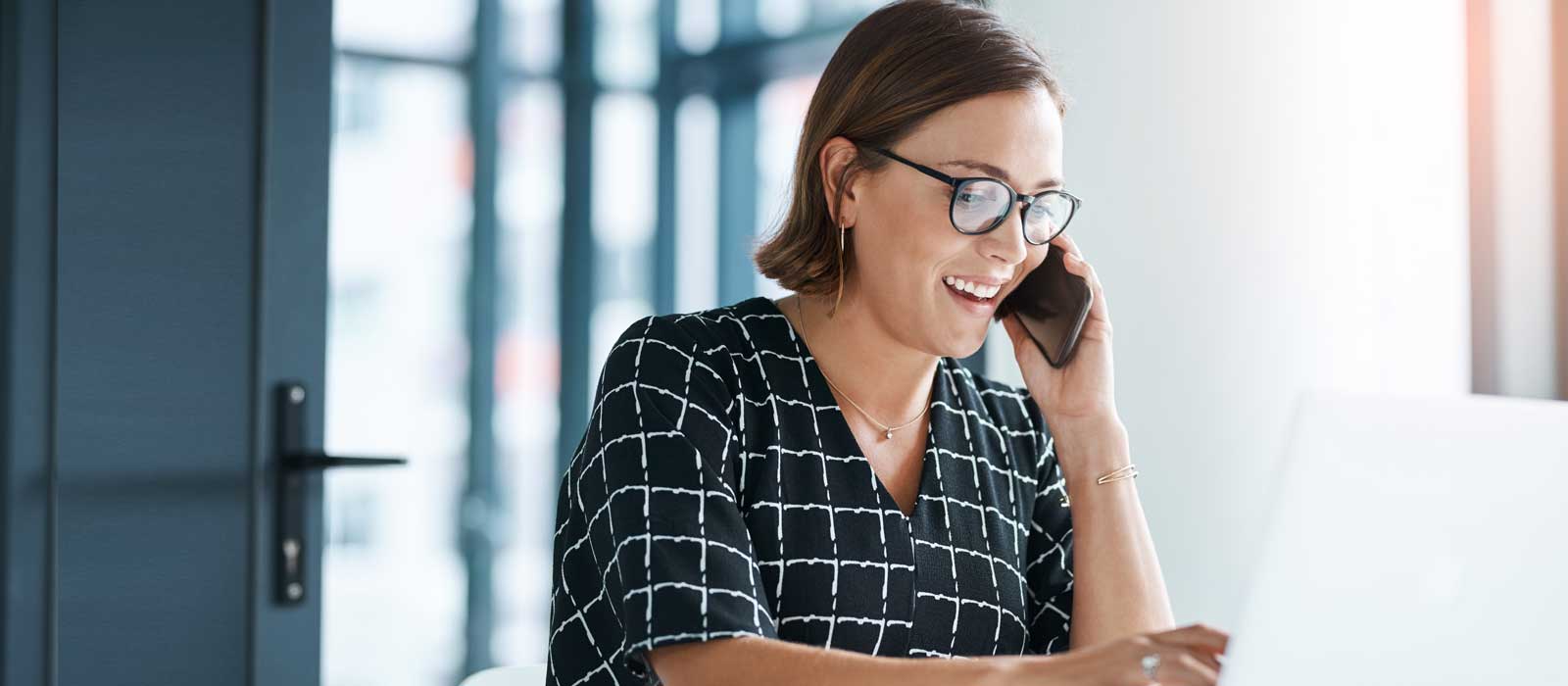 Woman talking on smartphone and using laptop