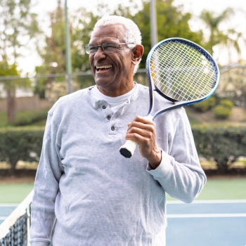 a man holding a tennis racket, smiling on a tennis court