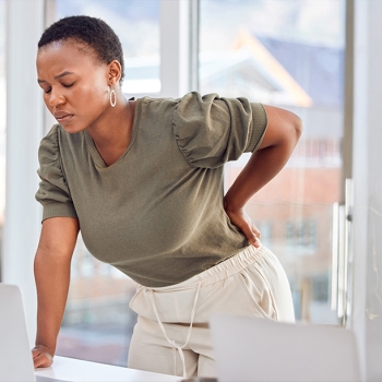 Diverse woman with back pain front of laptop