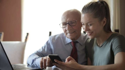 grandfather and granddaughter looking at phone and laptop together