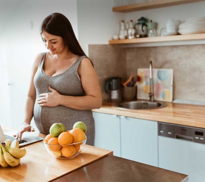 Pregnant woman viewing laptop in kitchen.
