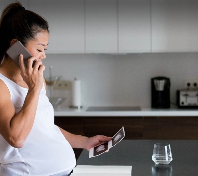 Pregnant woman on phone viewing sonogram image in kitchen.