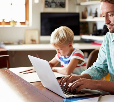 Father using laptop with young son next to him.