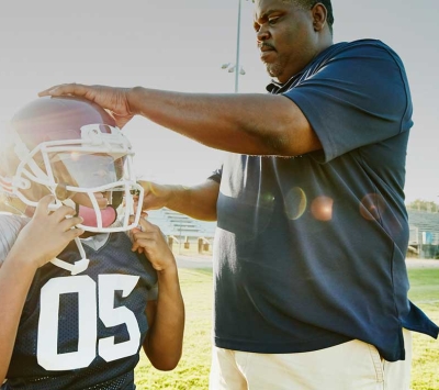 Youth football player's parent help with helmet