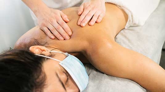 woman with mask getting a back massage