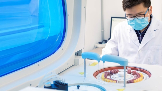 Researcher working in lab wearing PPE and looking at images