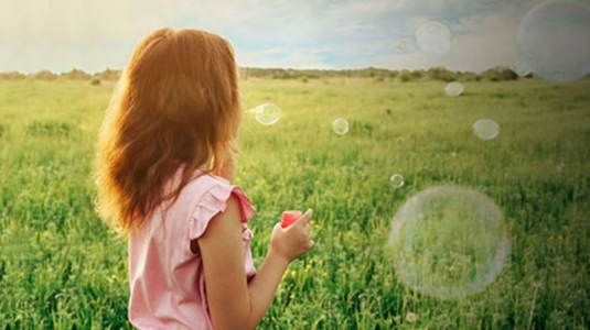 Girl blowing bubbles in field.