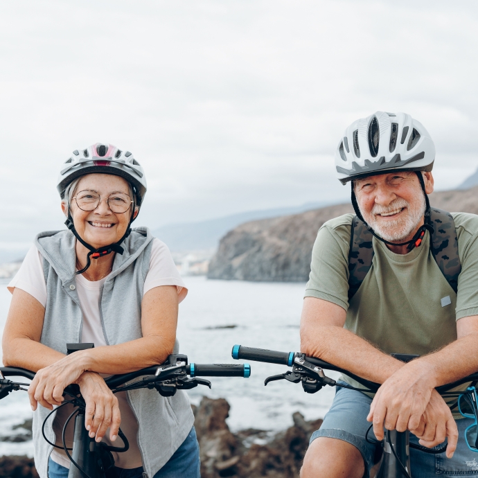 two seniors with light skin on the beach riding bikes